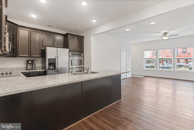 kitchen with light stone counters, a sink, dark wood-type flooring, dark brown cabinetry, and appliances with stainless steel finishes