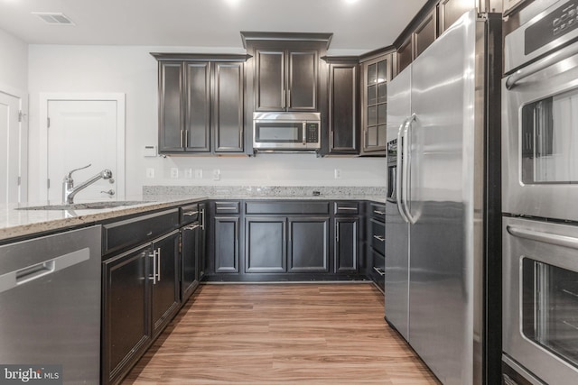 kitchen with light stone counters, visible vents, light wood-style flooring, a sink, and appliances with stainless steel finishes