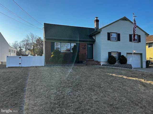 tri-level home featuring fence, a front yard, a garage, brick siding, and a chimney