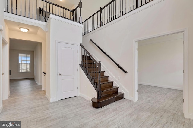 stairway featuring a towering ceiling, baseboards, and wood finished floors