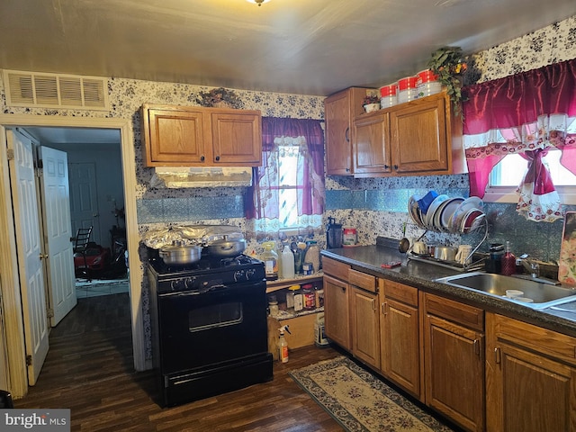 kitchen featuring under cabinet range hood, a sink, visible vents, gas stove, and dark wood finished floors