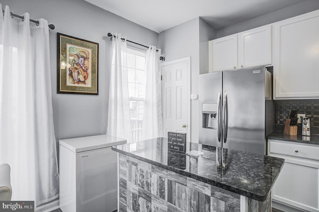 kitchen with dark stone counters, stainless steel fridge with ice dispenser, white cabinets, fridge, and backsplash