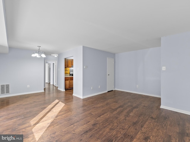 unfurnished living room featuring an inviting chandelier, baseboards, visible vents, and dark wood-style flooring