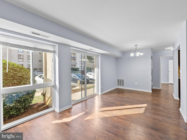 interior space with baseboards, wood finished floors, visible vents, and a notable chandelier