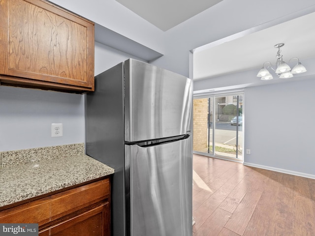 kitchen with light stone counters, light wood-style flooring, freestanding refrigerator, a chandelier, and baseboards