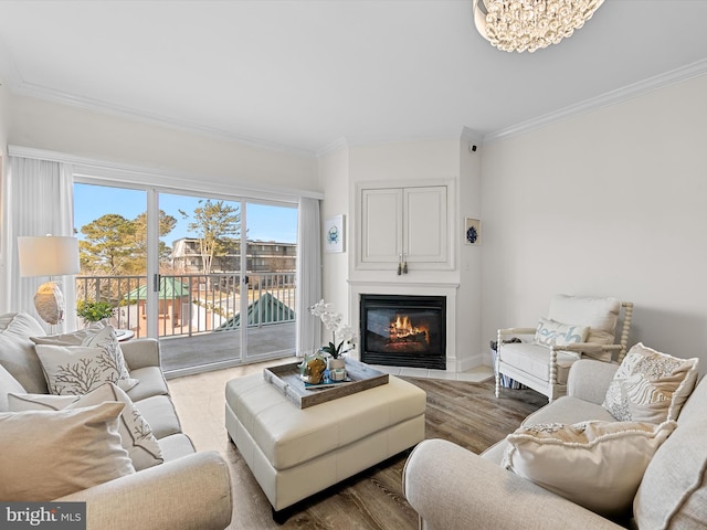 living area with a notable chandelier, wood finished floors, crown molding, and a glass covered fireplace