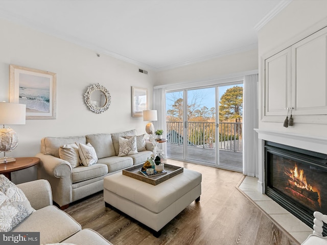 living room featuring ornamental molding, light wood-type flooring, a fireplace with flush hearth, and visible vents