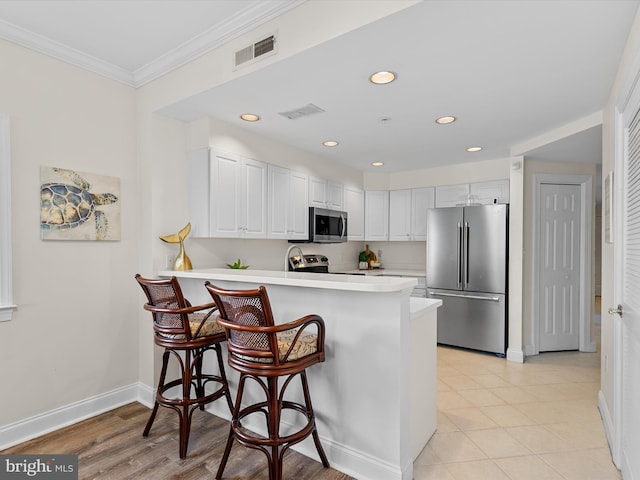 kitchen with visible vents, ornamental molding, a peninsula, stainless steel appliances, and light countertops