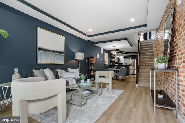 living area featuring brick wall, stairway, a tray ceiling, recessed lighting, and wood finished floors