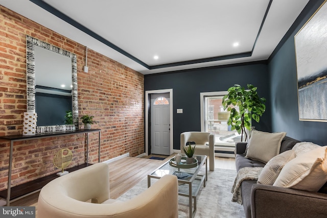 living area with brick wall, a tray ceiling, and wood finished floors