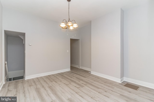 unfurnished room with baseboards, light wood finished floors, visible vents, and a notable chandelier