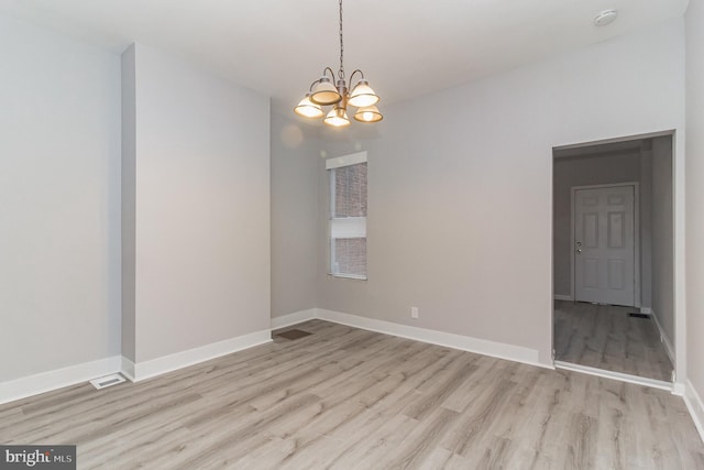 empty room with visible vents, light wood-style flooring, baseboards, and an inviting chandelier