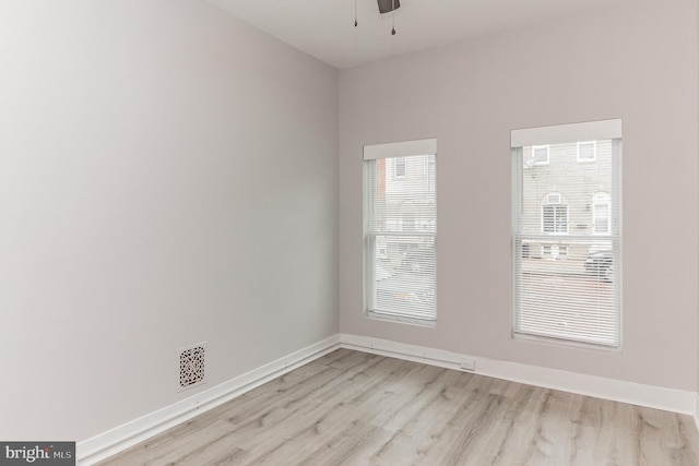 unfurnished room with visible vents, light wood finished floors, a ceiling fan, and baseboards