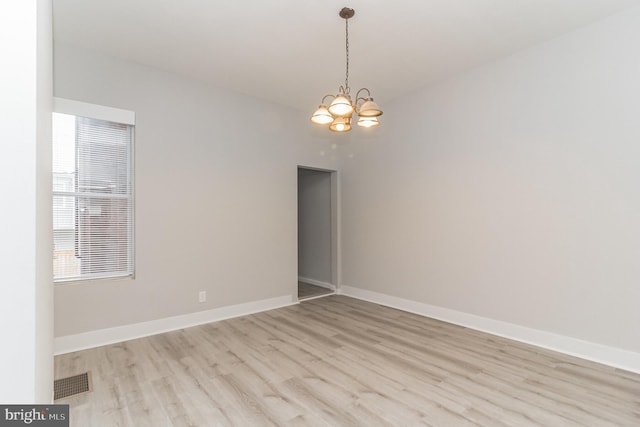 spare room featuring a chandelier, light wood-style floors, visible vents, and baseboards