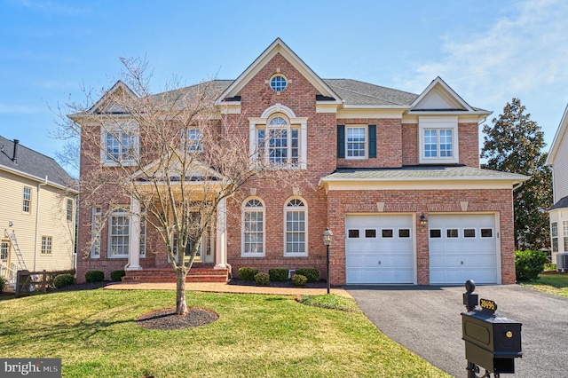 colonial home with a front lawn, driveway, an attached garage, a shingled roof, and brick siding