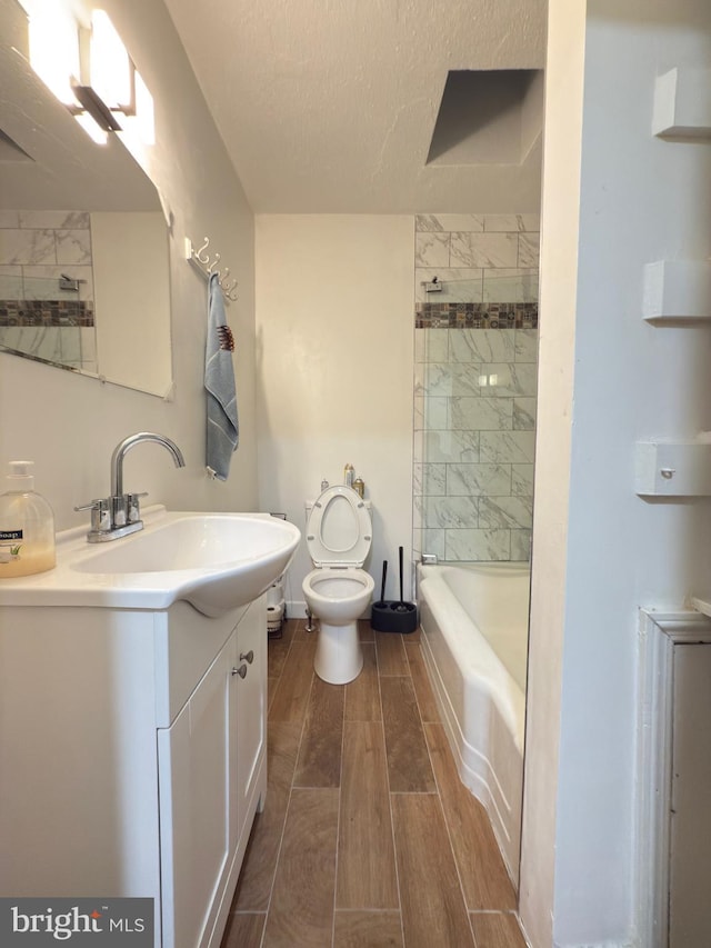 full bathroom with toilet, wood tiled floor, vanity, a textured ceiling, and baseboards