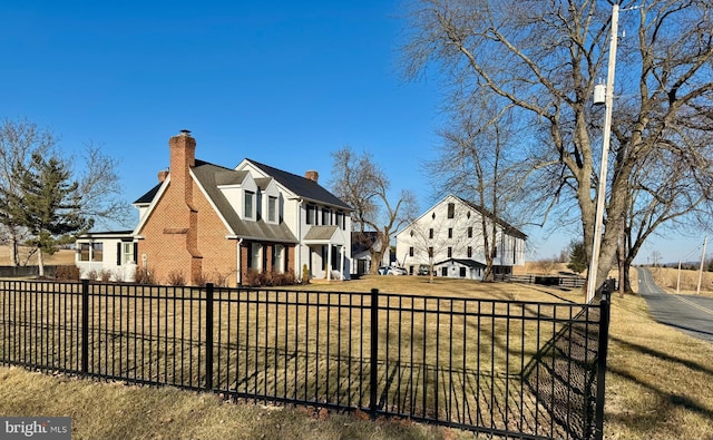 view of front facade with a fenced front yard, a front yard, brick siding, and a chimney