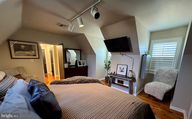 bedroom featuring baseboards, visible vents, vaulted ceiling, and wood finished floors