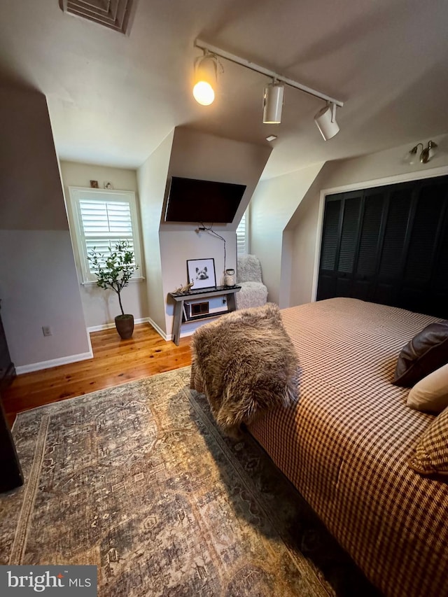 bedroom with rail lighting, visible vents, baseboards, and wood finished floors