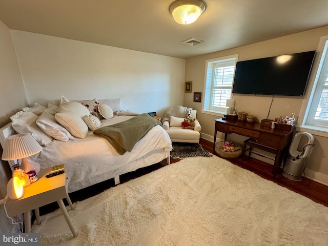 bedroom with multiple windows, wood finished floors, visible vents, and baseboards