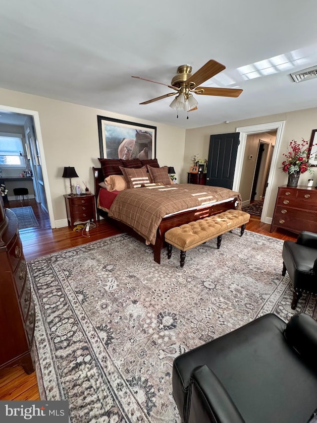 bedroom featuring a ceiling fan, wood finished floors, visible vents, and baseboards