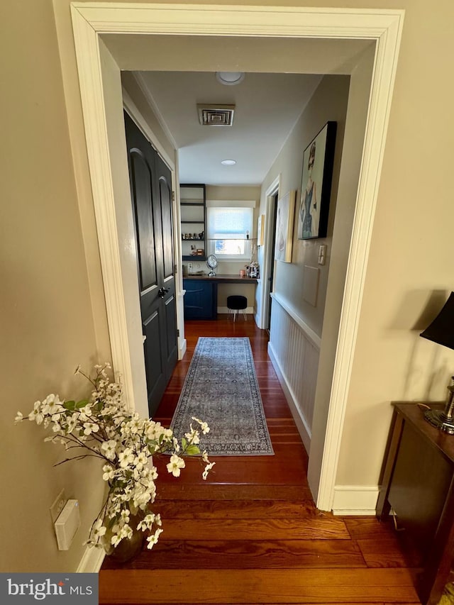 hallway featuring baseboards, visible vents, and dark wood finished floors