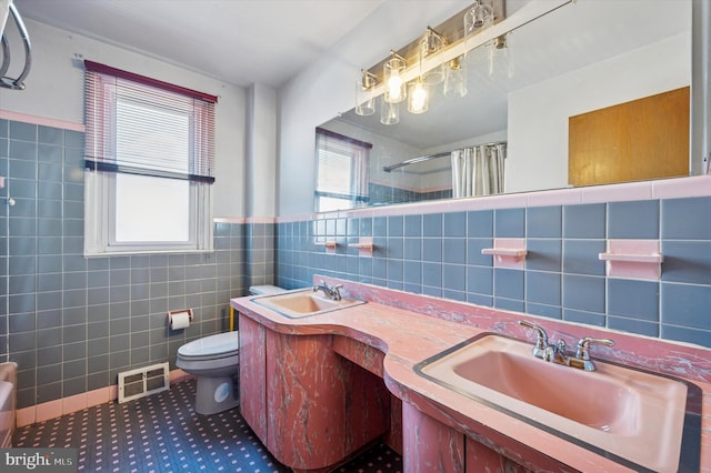 bathroom featuring tile walls, toilet, visible vents, and a sink