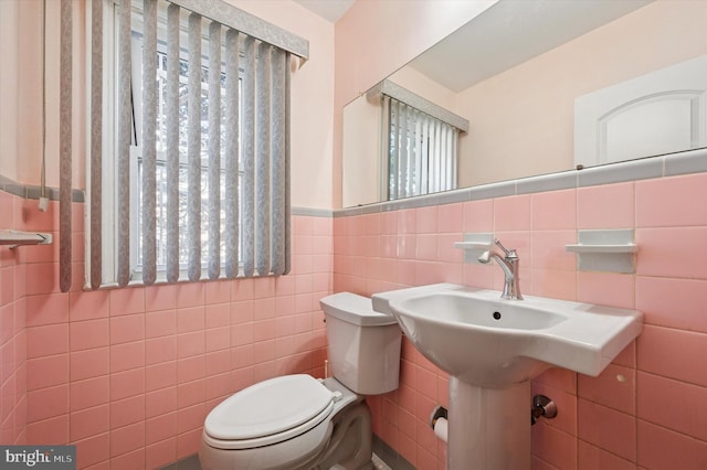 half bathroom featuring tile walls, toilet, a healthy amount of sunlight, and wainscoting