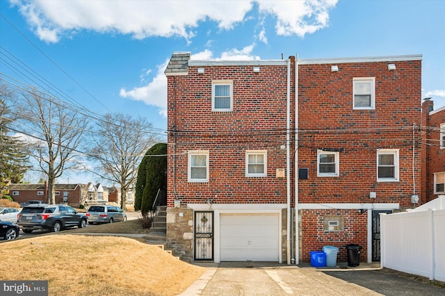 rear view of property featuring a lawn, driveway, fence, a garage, and brick siding