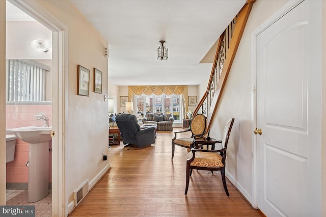 hall with stairs, tile walls, light wood-style flooring, and visible vents