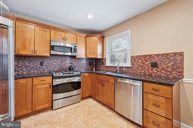 kitchen featuring backsplash, stainless steel appliances, dark stone counters, and a sink