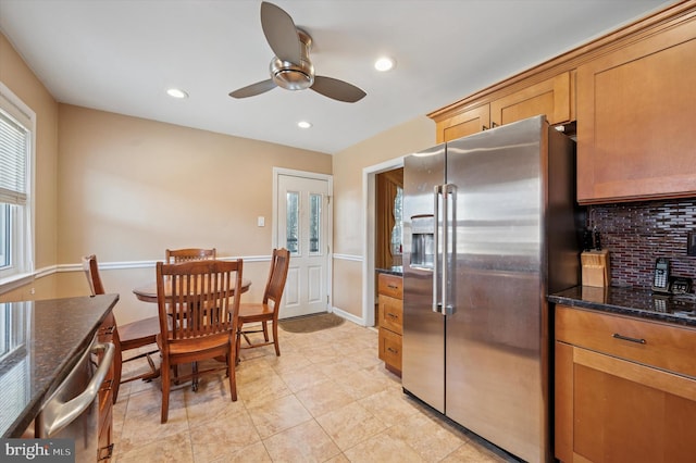 kitchen with a ceiling fan, stainless steel refrigerator with ice dispenser, recessed lighting, dark stone counters, and decorative backsplash