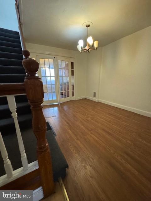 unfurnished dining area with stairs, baseboards, wood finished floors, and a chandelier