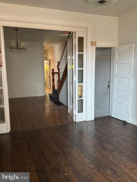 empty room with stairs, a notable chandelier, and wood finished floors