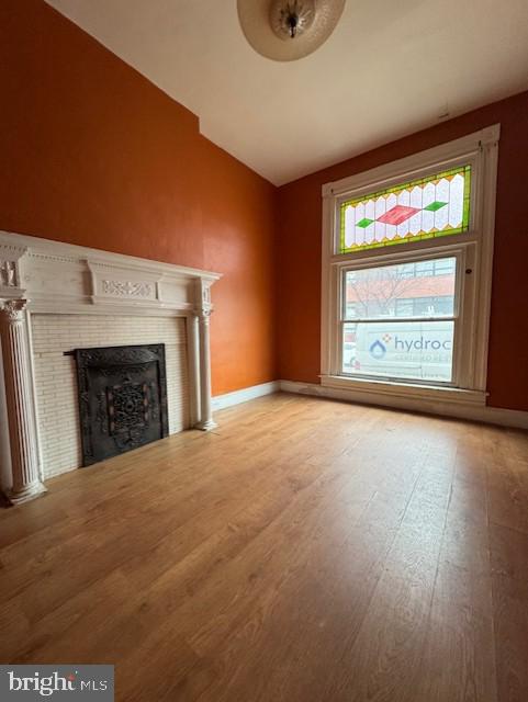 unfurnished living room with a fireplace, baseboards, vaulted ceiling, and wood finished floors