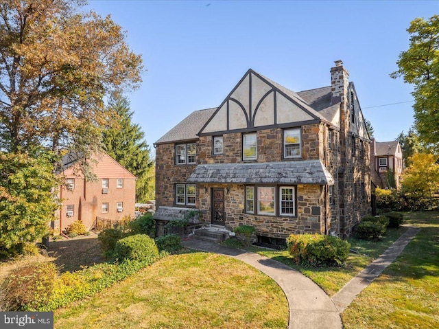 tudor house with a front yard, a chimney, and stucco siding