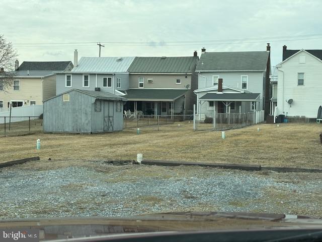 rear view of house featuring an outbuilding, a yard, a storage unit, fence, and a residential view