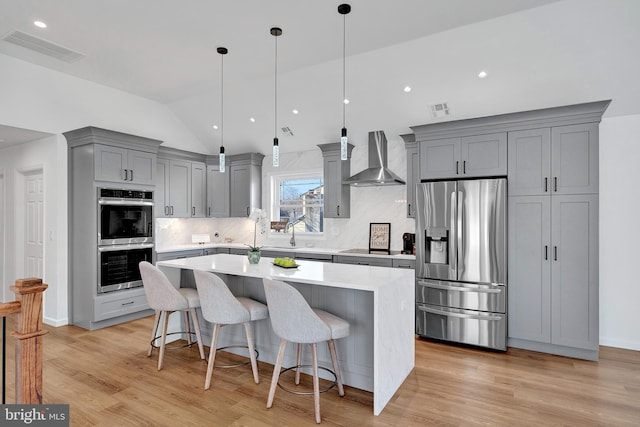 kitchen featuring gray cabinets, visible vents, appliances with stainless steel finishes, a kitchen island, and wall chimney exhaust hood