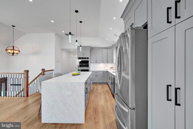 kitchen with gray cabinetry, stainless steel appliances, a kitchen island, light wood finished floors, and tasteful backsplash