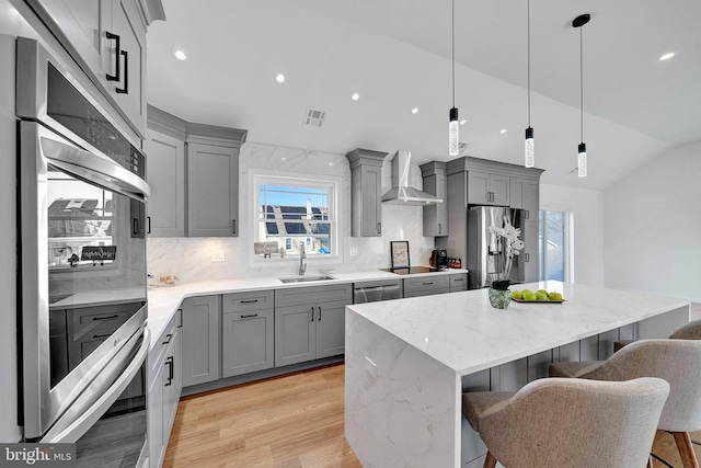 kitchen featuring wall chimney exhaust hood, appliances with stainless steel finishes, a sink, and gray cabinetry