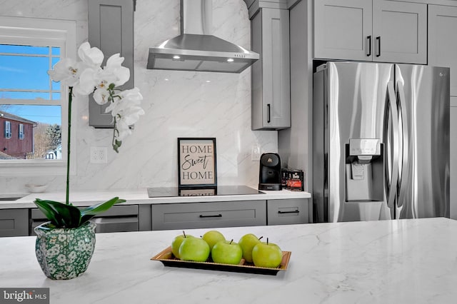 kitchen with black electric stovetop, decorative backsplash, gray cabinetry, wall chimney range hood, and stainless steel fridge