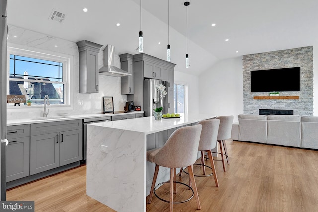 kitchen with light wood finished floors, appliances with stainless steel finishes, gray cabinetry, wall chimney range hood, and a sink