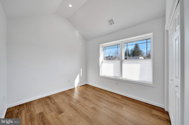 spare room featuring baseboards, visible vents, vaulted ceiling, and wood finished floors