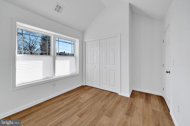 unfurnished bedroom featuring lofted ceiling, light wood-style flooring, visible vents, baseboards, and a closet