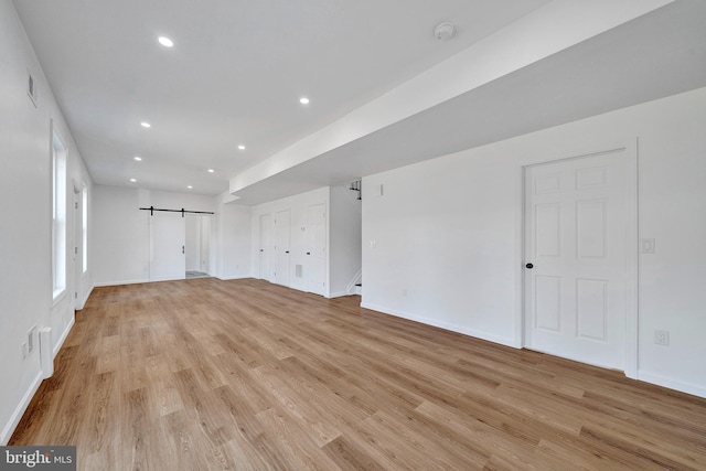 interior space with light wood-type flooring, a barn door, baseboards, and recessed lighting