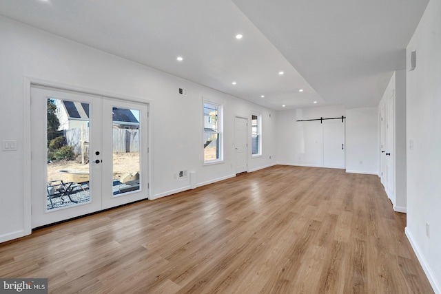 unfurnished living room featuring recessed lighting, light wood finished floors, a barn door, and french doors