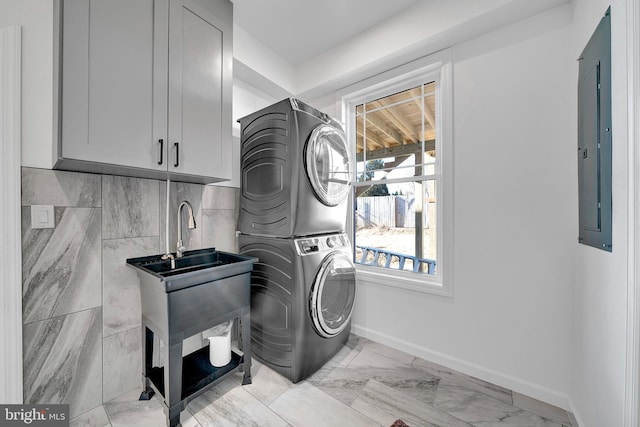 clothes washing area featuring marble finish floor, stacked washer / dryer, laundry area, electric panel, and baseboards