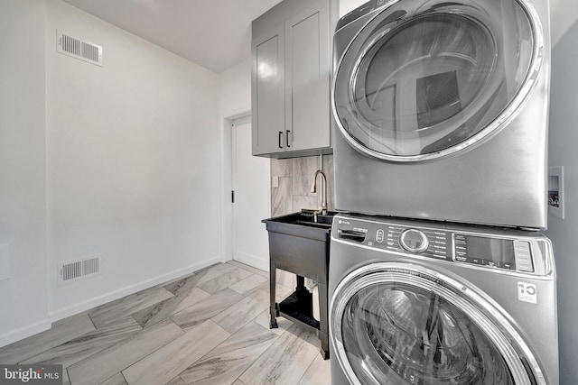 laundry room featuring stacked washer and clothes dryer, cabinet space, visible vents, and baseboards