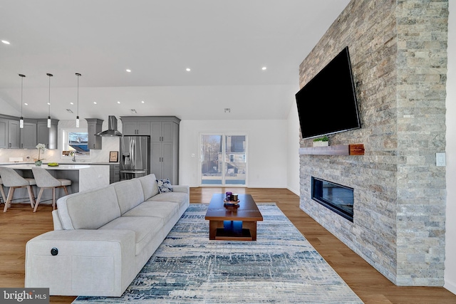 living area featuring recessed lighting, wood finished floors, and a stone fireplace