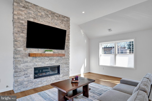 living room featuring baseboards, visible vents, wood finished floors, and a stone fireplace